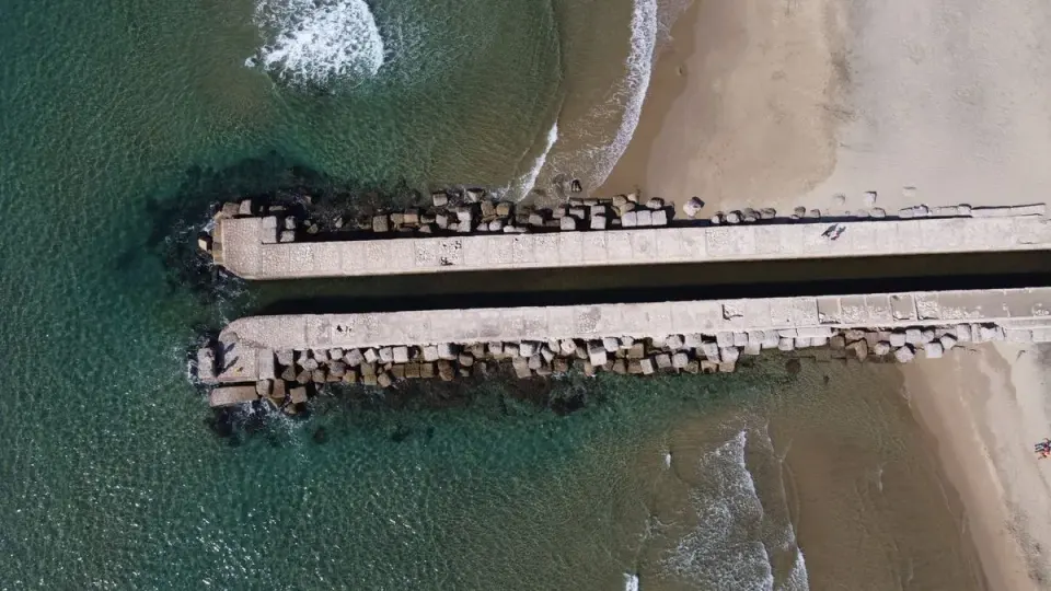 Aerial perspective of a concrete pier extending into the sea at Anzio's coastline in Italy. -…