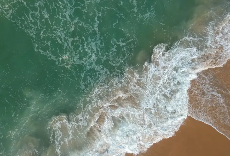 Captivating aerial view of ocean waves crashing onto a sandy shore, showcasing nature's beauty.…