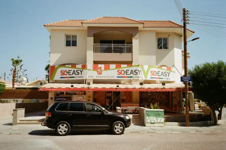 Street view of a convenience store in Cyprus with a black SUV parked outside. - Photo by Liza…