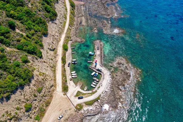 A stunning aerial view of Kerkira's rocky coastline, featuring anchored boats and clear…