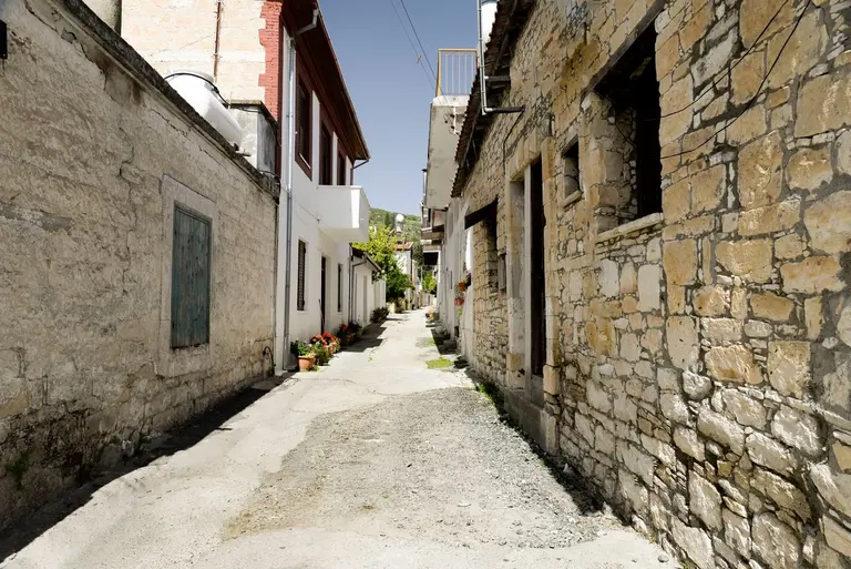 Explore the rustic charm of a narrow alley flanked by stone buildings in a peaceful Cypriot…