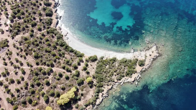 A stunning aerial shot of a Greek coastline with clear blue waters and lush greenery. - Photo by…