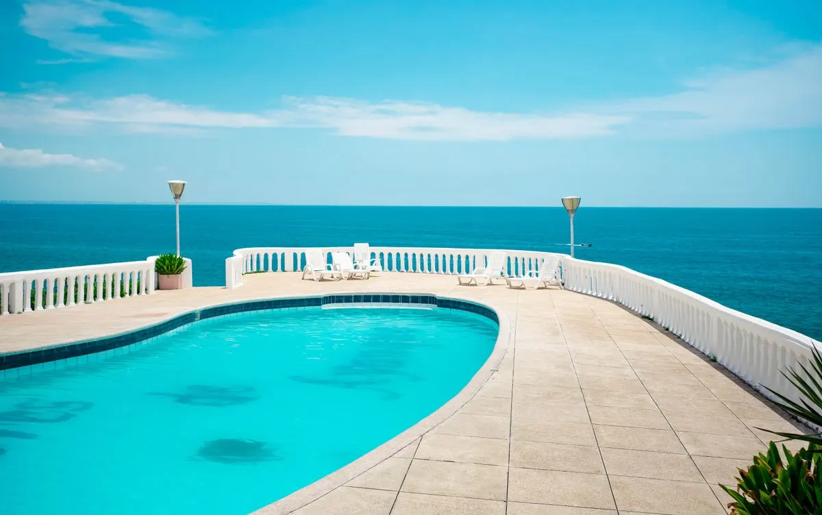 A tranquil swimming pool at a seaside resort with ocean views under a clear blue sky. - Photo by…