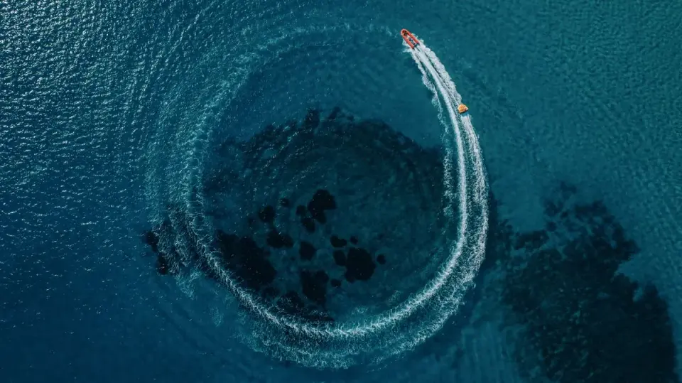 Aerial shot of a speedboat creating a circular wave pattern in the clear blue waters of Alaçatı,…