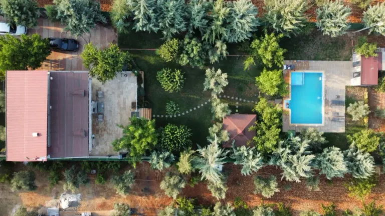 Top-down aerial shot of a villa with a swimming pool amidst trees, showcasing elegant outdoor…