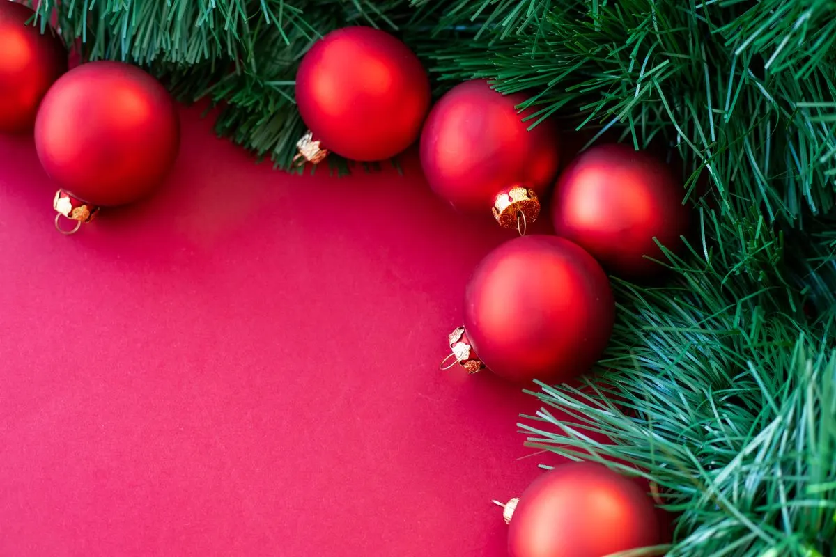 Bright red Christmas ornaments nestled among lush green pine leaves, perfect for festive…