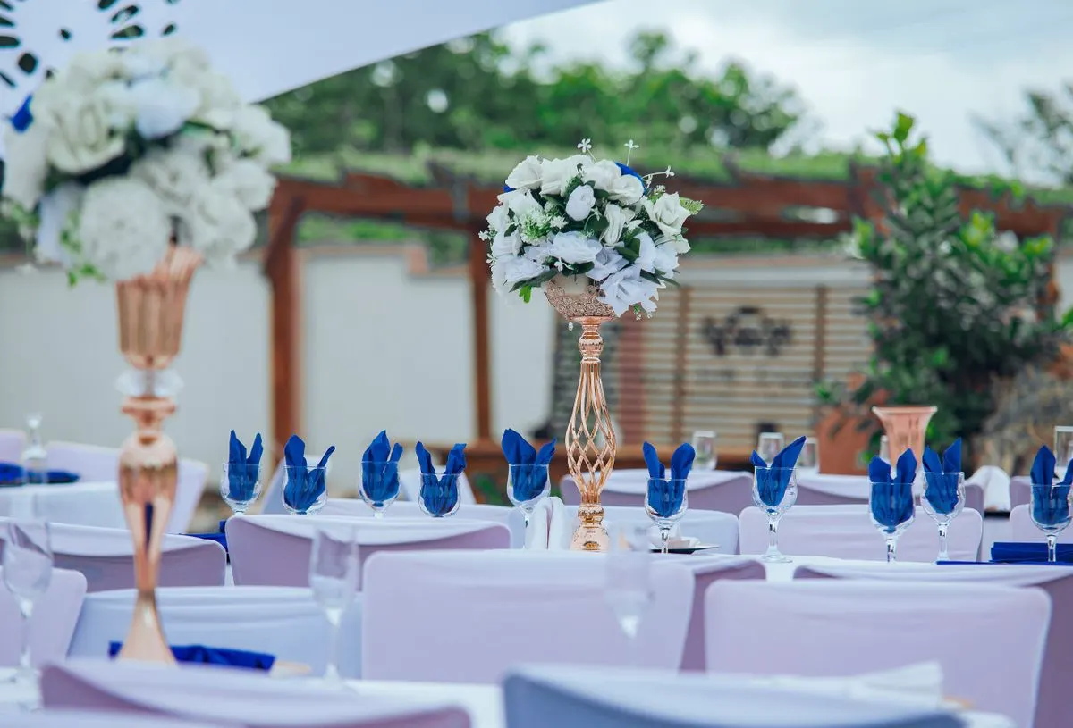 A beautifully decorated outdoor dinner setting with white flowers and blue accents. - Photo by…