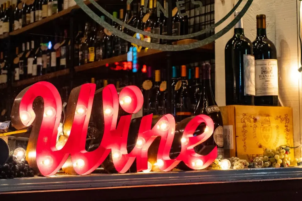 Illuminated wine sign with bottles and grapes create a lively ambiance in a liquor store window.…