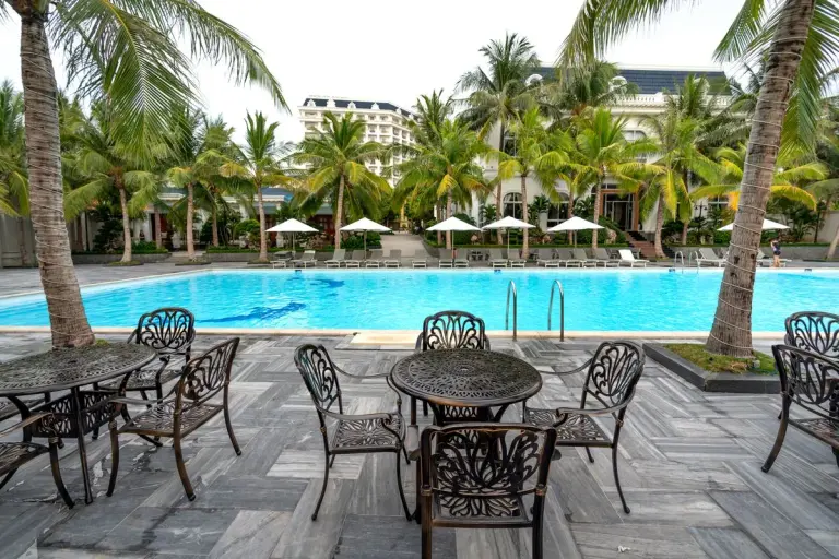 Elegant poolside area with palm trees, tables, and sun loungers, perfect for relaxation. - Photo…