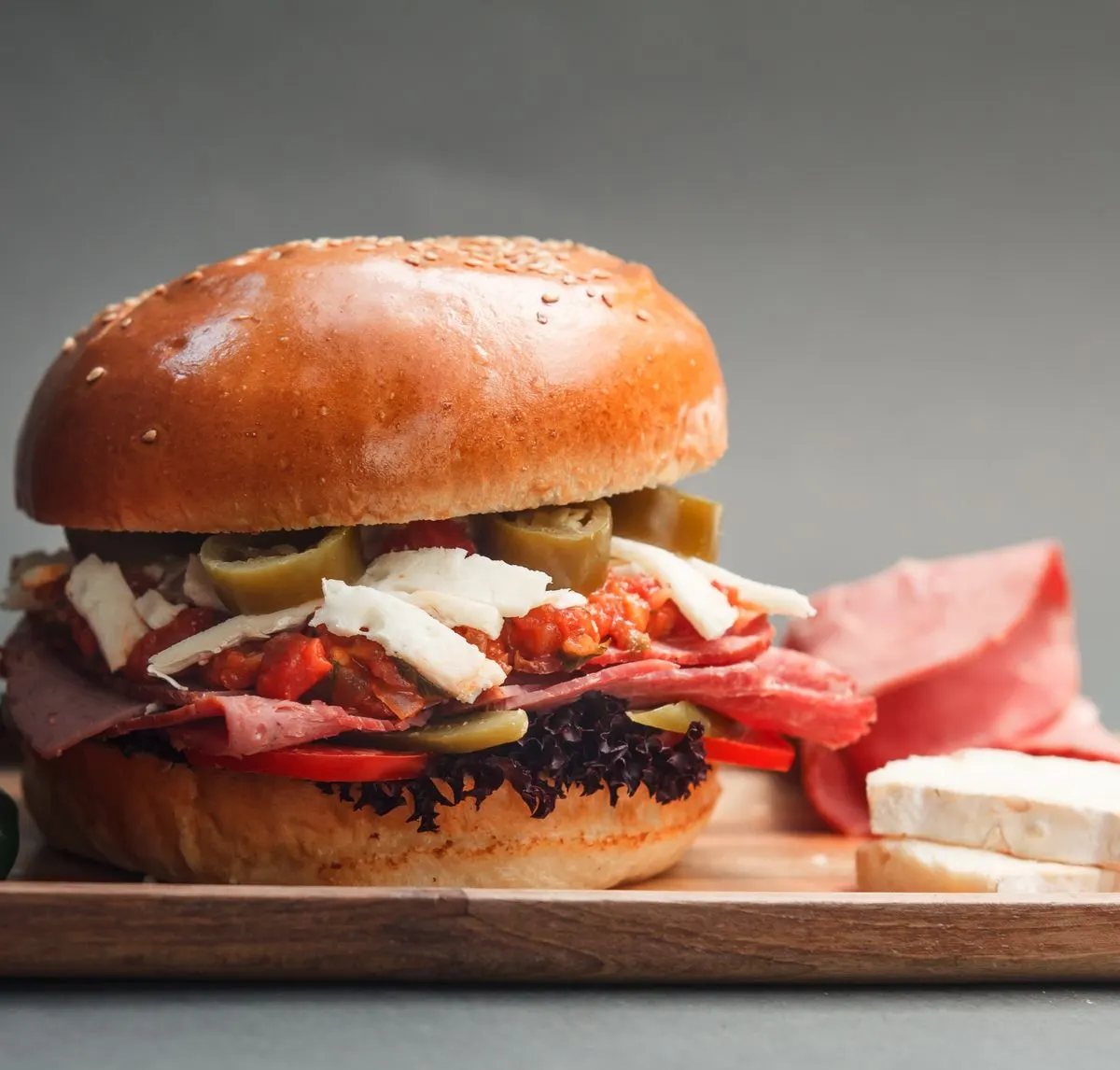 Close-up of a gourmet sandwich with cheese, ham, and vegetables on a cutting board. - Photo by…