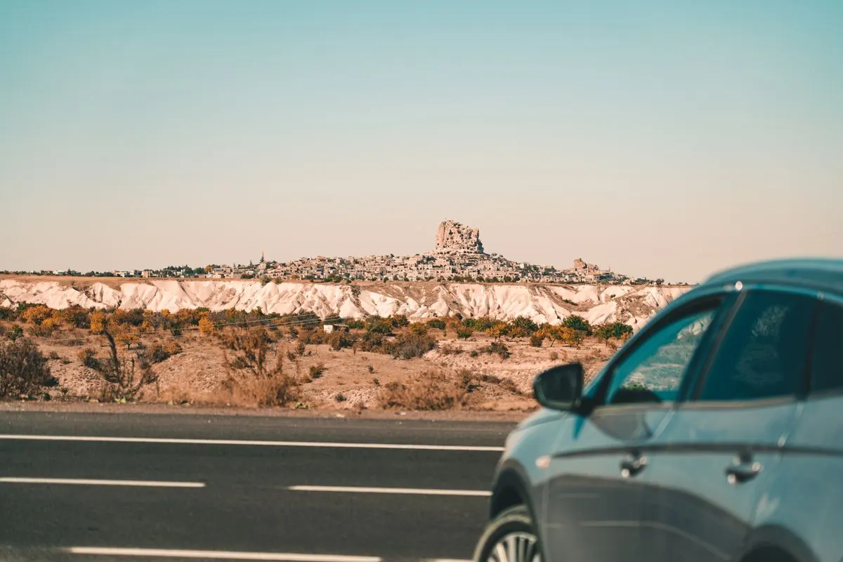 Scenic view of Uchisar Castle in Cappadocia with a car on the road in the foreground. - Photo by…