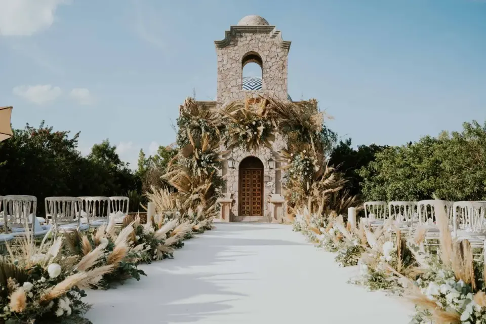 Beautiful outdoor wedding aisle with floral decorations leading to a stone building under a…