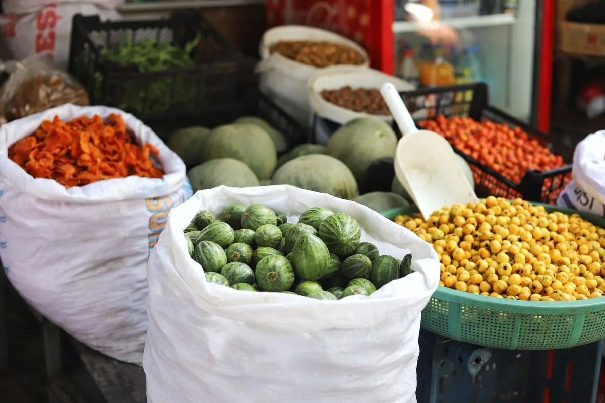 A variety of vegetables and fruits displayed in sacks and baskets at an outdoor market stall. -…