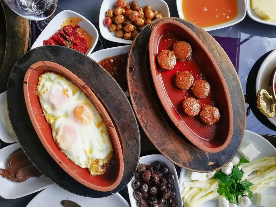 Top view of a traditional Turkish breakfast featuring eggs, meatballs, and assorted meze dishes.…