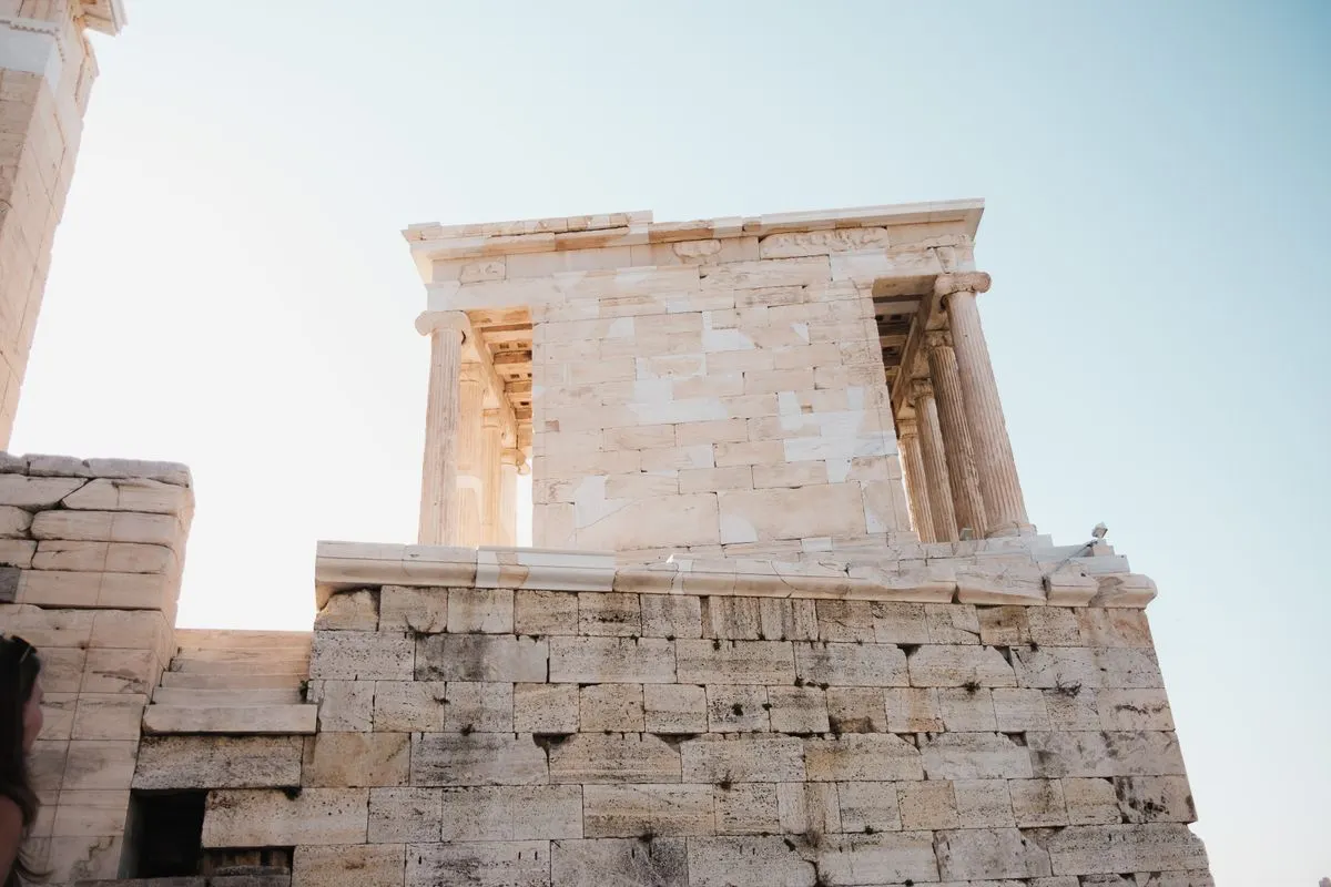 View of the ancient Temple of Athena Nike in Athens, Greece under a clear blue sky. - Photo by…