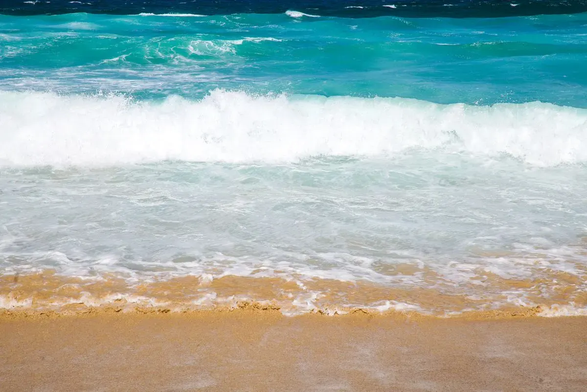 Captivating view of turquoise ocean waves gently lapping on a sunny sandy beach, perfect for…