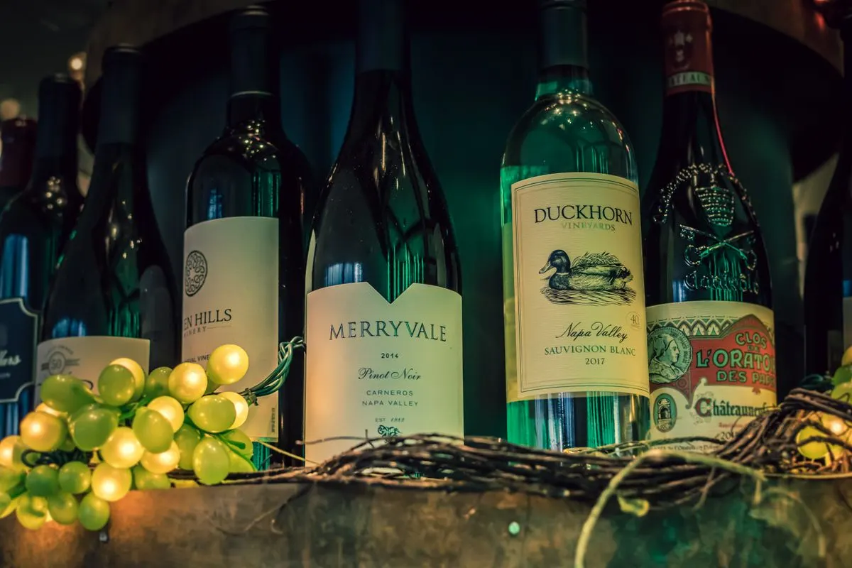Close-up of wine bottles with green grapes, perfect for wine enthusiasts. - Photo by Brett…