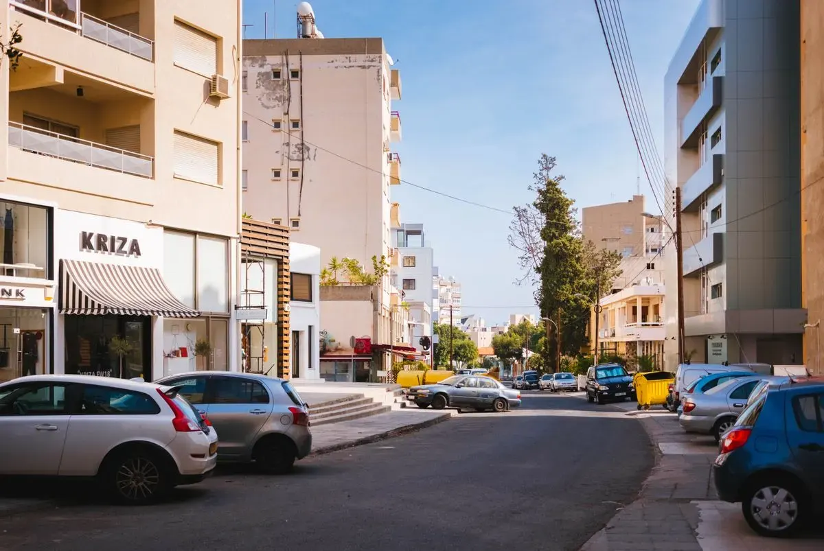 Sunlit street in a Mediterranean city with cars and modern architecture. - Photo by Igor Starkov…