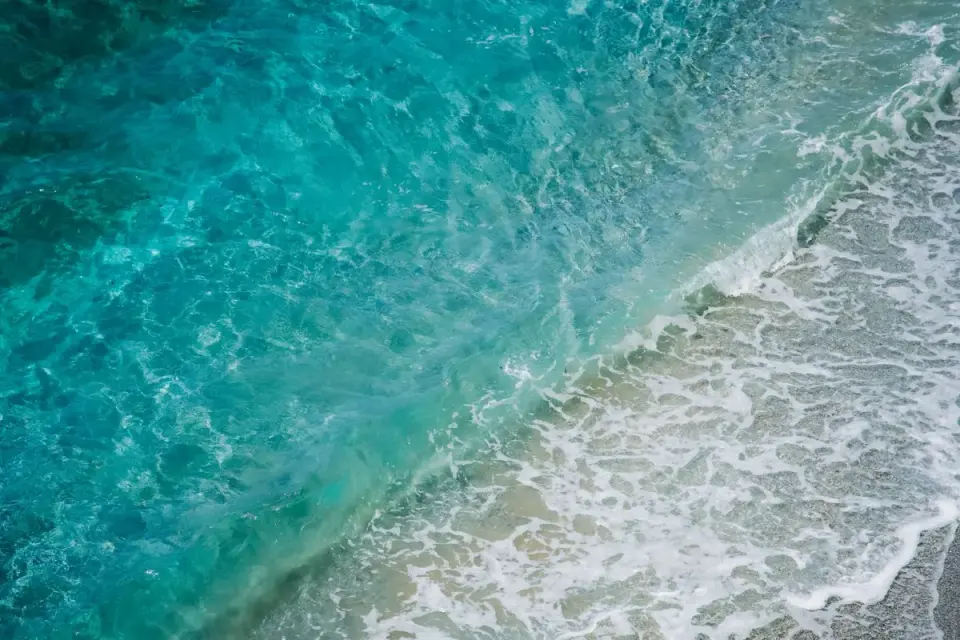Vibrant aerial view of turquoise ocean waves crashing onto a sandy shore, showcasing the beauty…