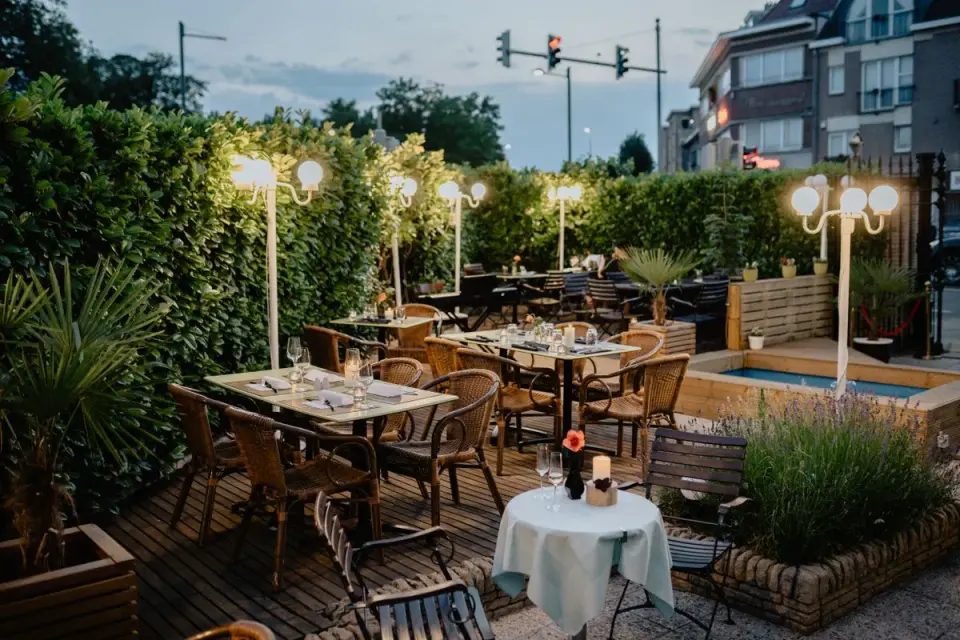 Inviting outdoor restaurant seating area with elegant lamps and lush greenery. - Photo by Boris…