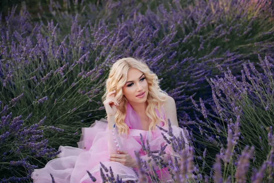 A blonde woman in a pink dress poses in a beautiful lavender field in Cyprus, epitomizing summer…