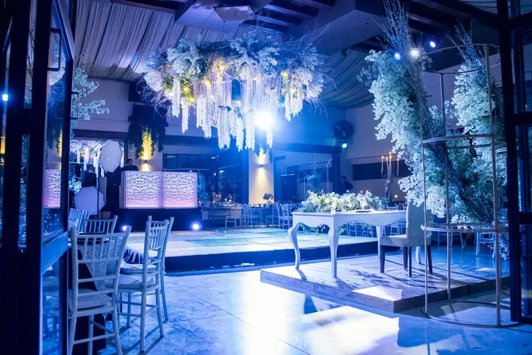 Beautifully decorated indoor wedding reception with elegant floral arrangements and lighting. -…