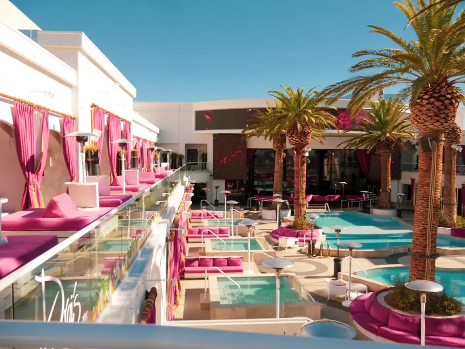 Elegant resort pool with vibrant pink accents and palm trees in bright daylight. - Photo by…