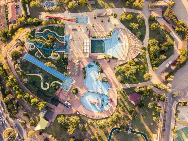 High-angle shot of a colorful waterpark with slides and pools, surrounded by greenery. - Photo…