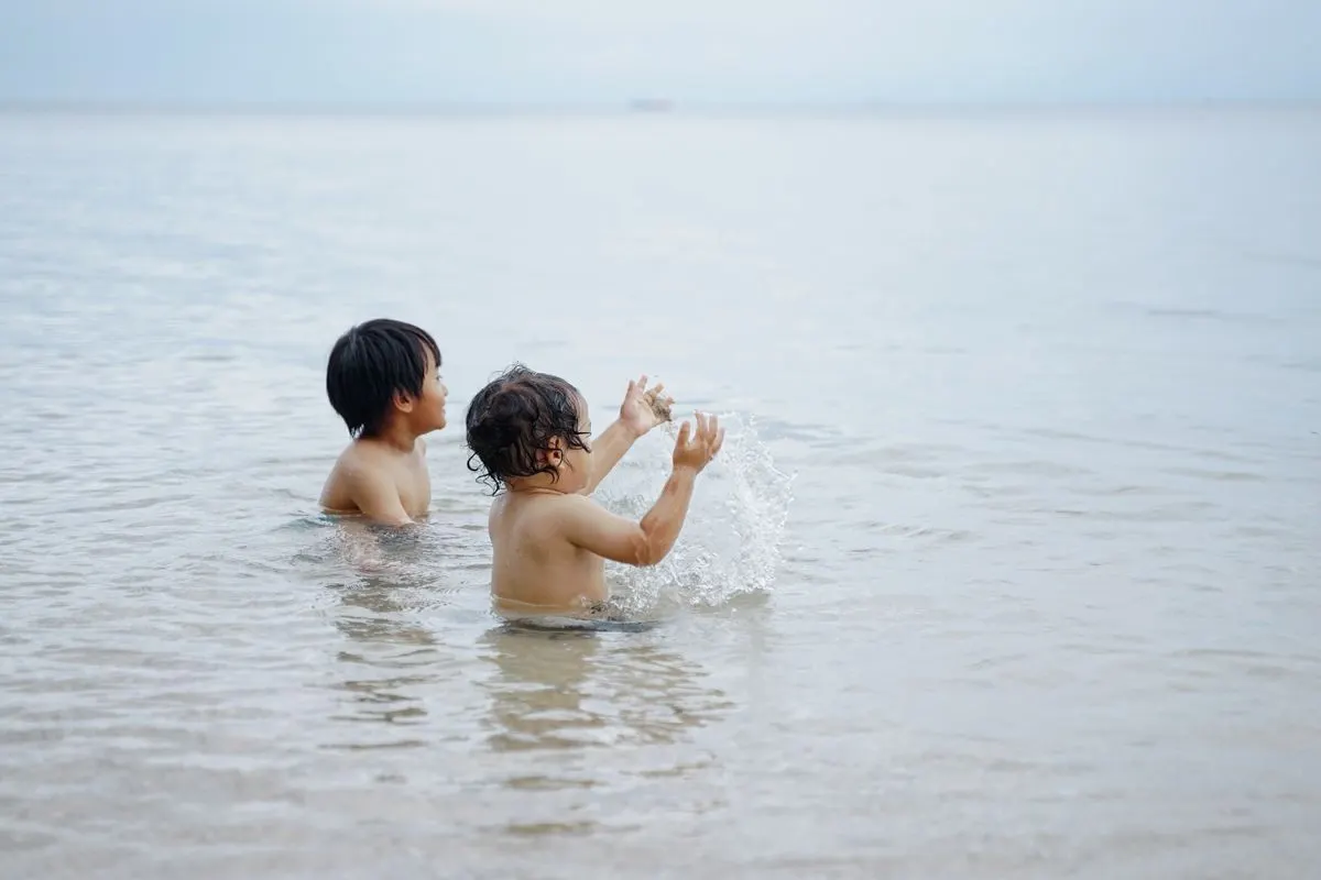 Two kids enjoying playful moments in the ocean at a private beach in Banyuwangi, Indonesia. -…