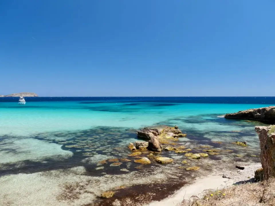 A breathtaking view of Ibiza's turquoise waters and rocky coastline under a clear blue sky. -…