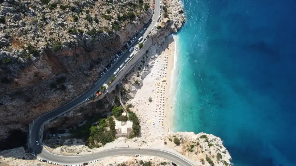 Breathtaking aerial view of a coastal beach with clear blue waters and a winding road along…