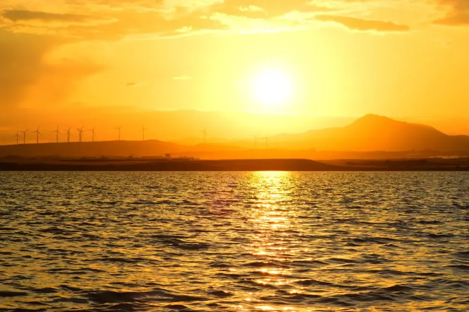 Stunning sunrise over Larnaca Bay with wind turbines and golden reflections on the water. -…