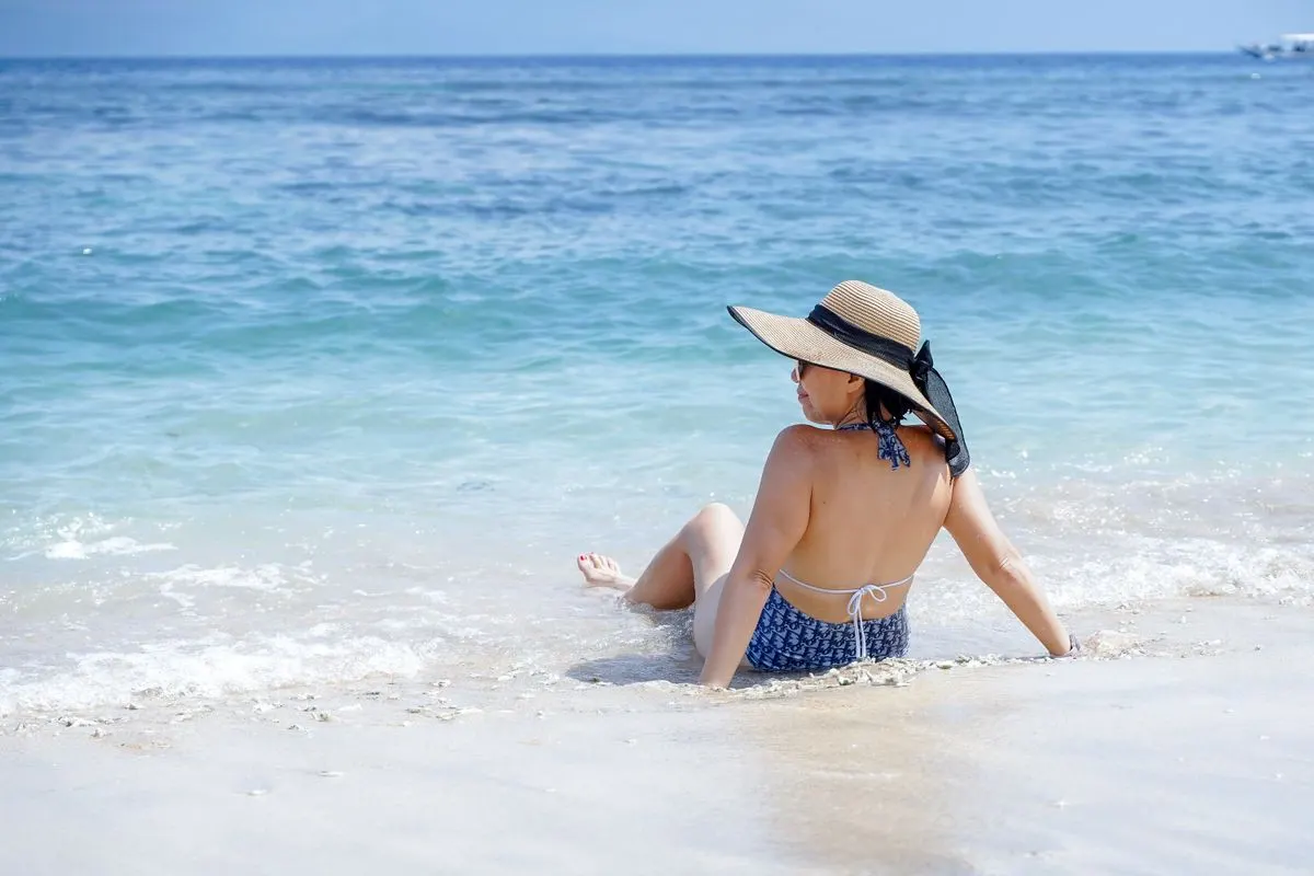 A woman relaxes on a sandy beach, enjoying the sunny summer day beside the ocean. - Photo by…