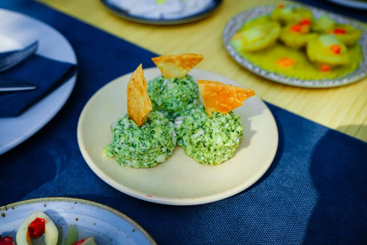 Plate of green cheese balls garnished with crispy chips on an outdoor table. - Photo by Busenur…