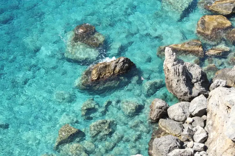 Aerial view of turquoise sea water and a rocky shoreline, captured in natural daylight. - Photo…