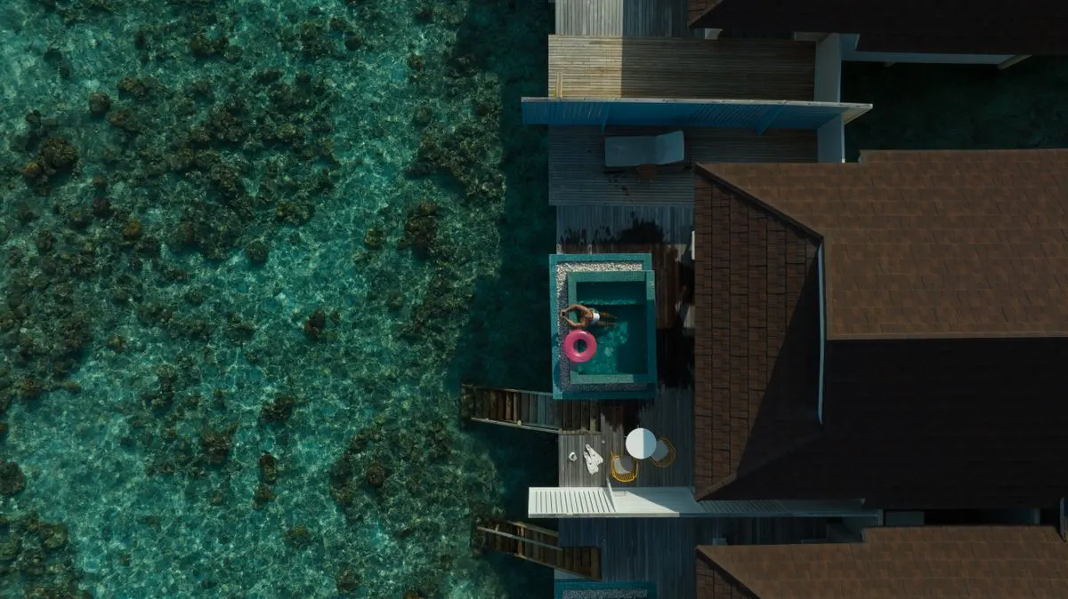 Stunning aerial view of a Maldives overwater villa with clear lagoon, featuring a bright pool…