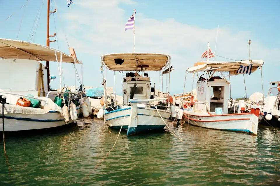 A scenic view of traditional fishing boats docked in Corfu, Greece under a clear blue sky. -…