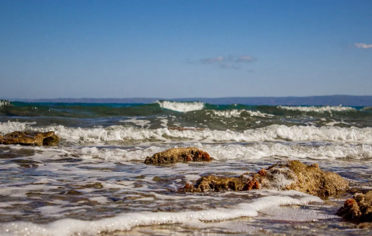 Waves gently splashing on the rocky shore in Hanioti, Greece under a clear blue sky. - Photo by…