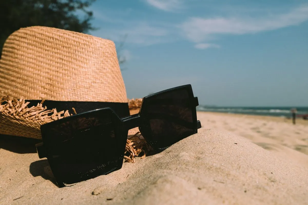 Sunglasses and straw hat resting on the sand with ocean backdrop on a sunny day, perfect for…