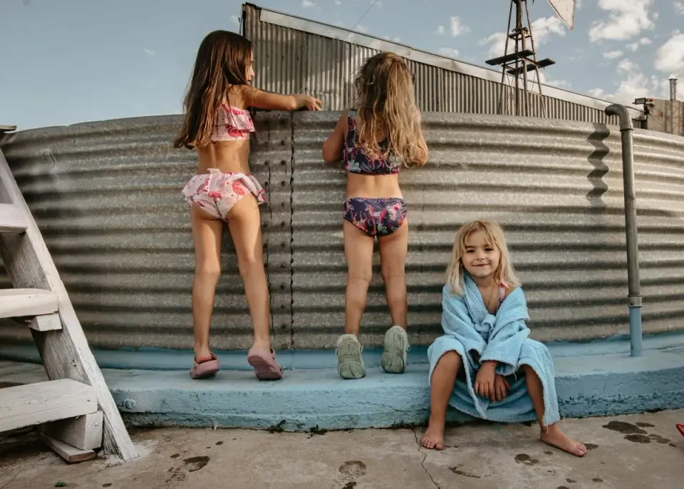 Tři děti si užívají slunečný den v plavkách u vodní nádrže. - Foto: Natalia Olivera dne…