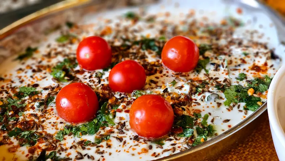 A vibrant yogurt dish topped with cherry tomatoes, herbs, and spices, perfect for culinary…
