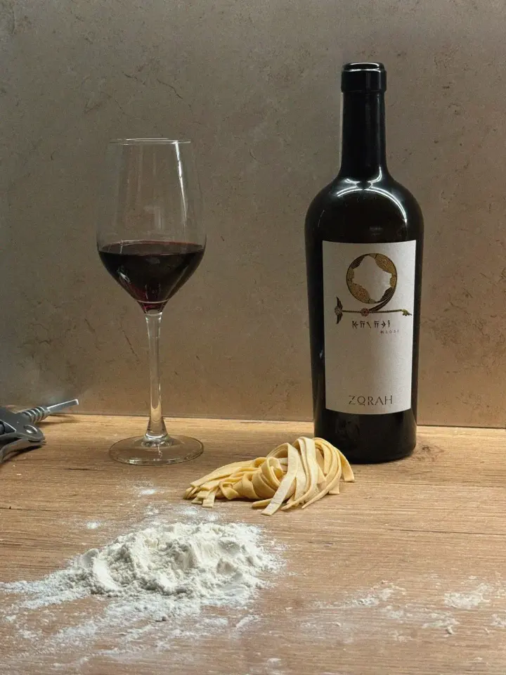 A bottle of wine in a bag with grapes and an empty glass on a rustic table, ideal for culinary…