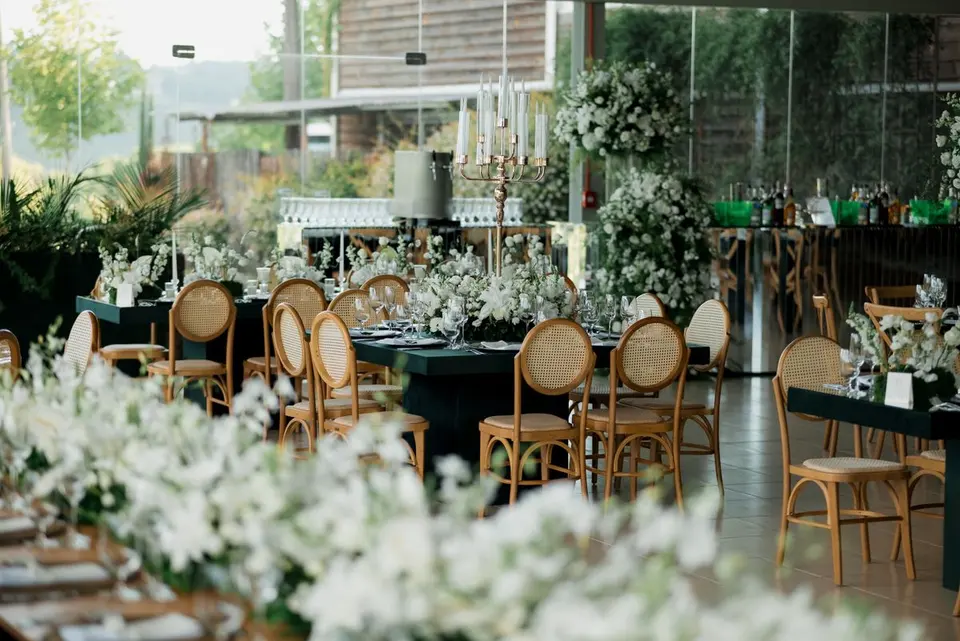 Chic event decoration with floral arrangements and wooden chairs in a bright sunlit room. -…