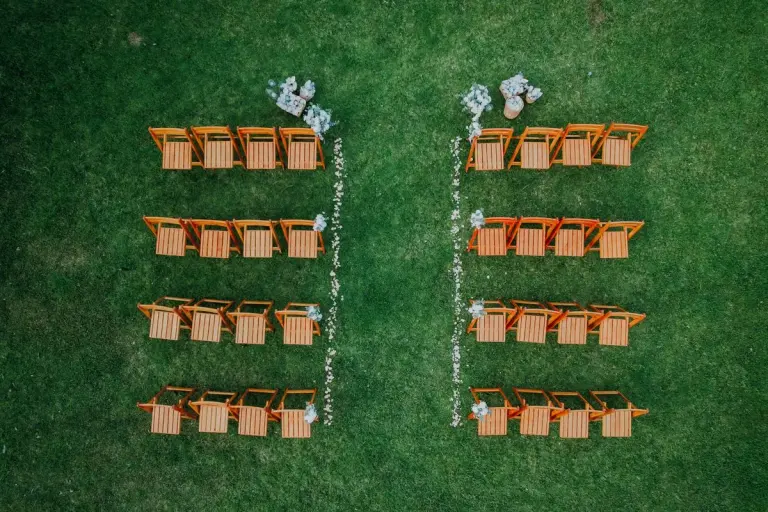 Drone shot of a wedding seating arrangement with orange chairs on green grass. - Photo by Leo…