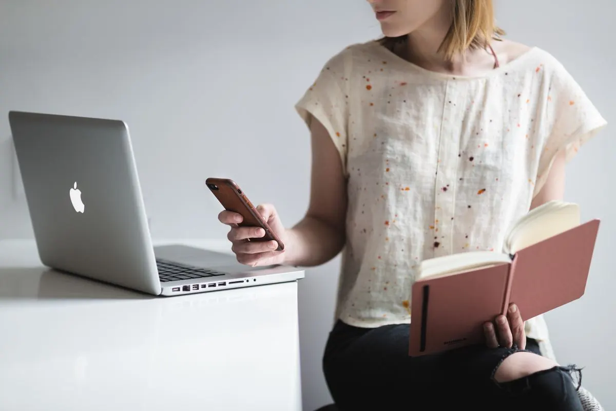 Woman working on a laptop while reading and texting, embodying modern multitasking. - Photo by…