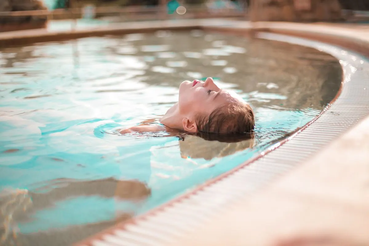 A woman enjoys peaceful relaxation while floating in a sunny outdoor pool, captured in soft…