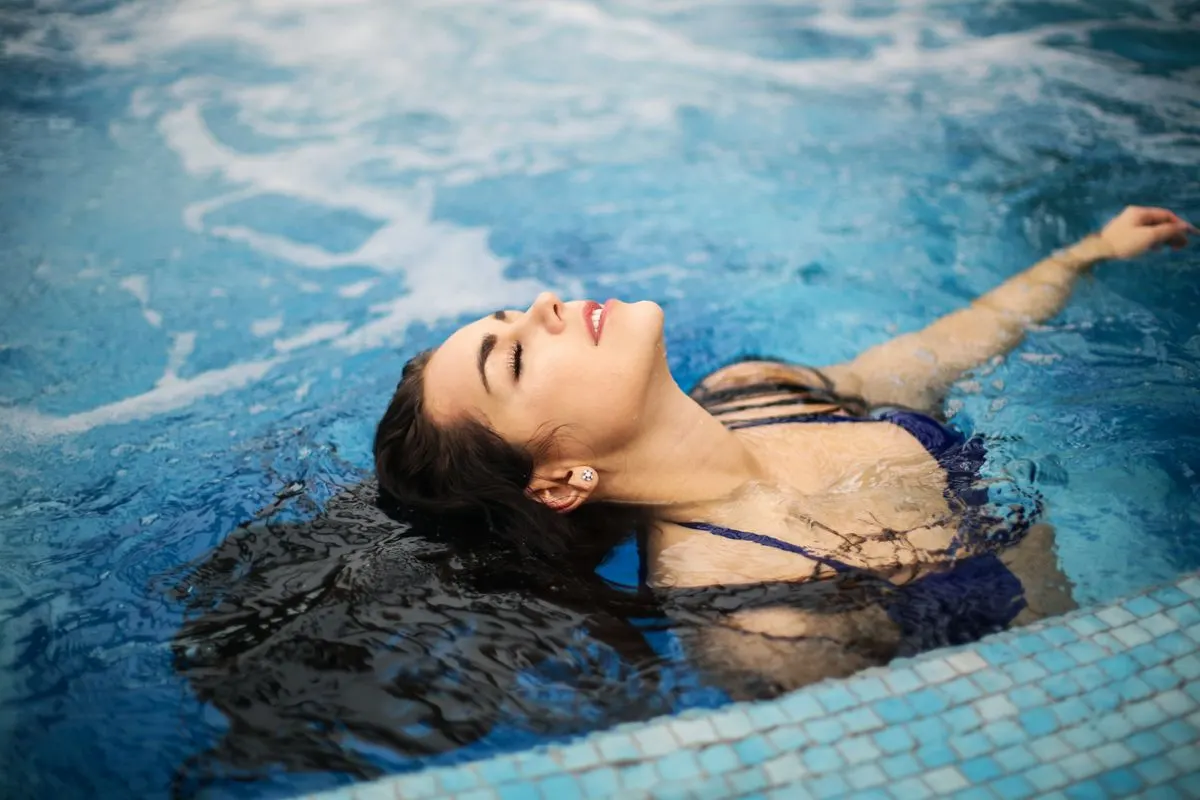 A woman enjoys a relaxing moment in a clear, blue swimming pool on a sunny day. - Photo by…