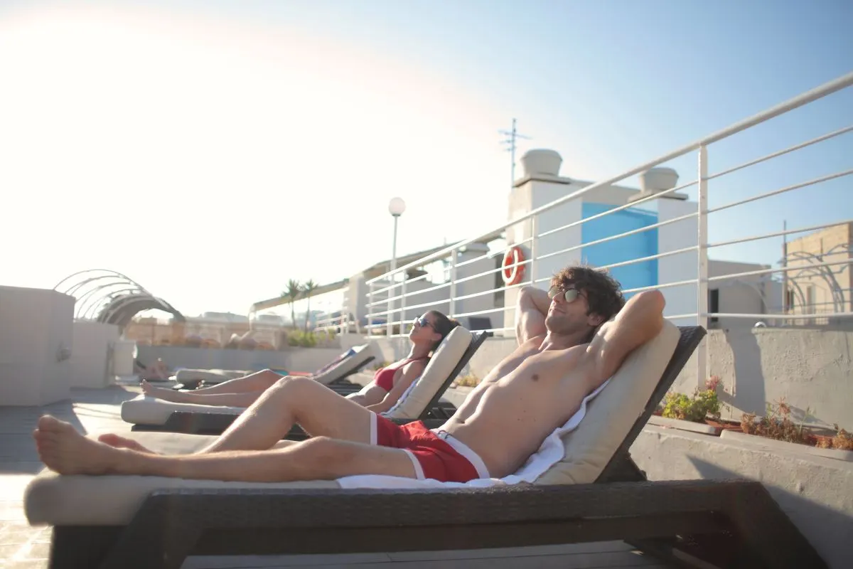 Side view of young man and woman in swimsuits and sunglasses relaxing on sun loungers together…