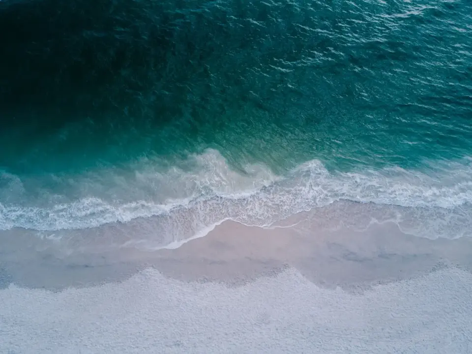 Stunning aerial shot of turquoise ocean waves washing onto a pristine sandy beach, perfect for…