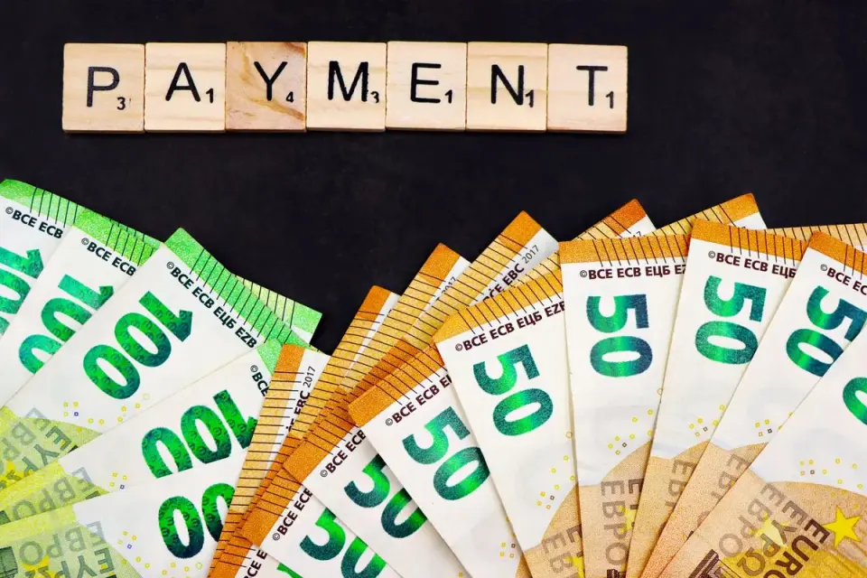 Euro banknotes fanned out with 'PAYMENT' spelled in Scrabble tiles, representing finance and…